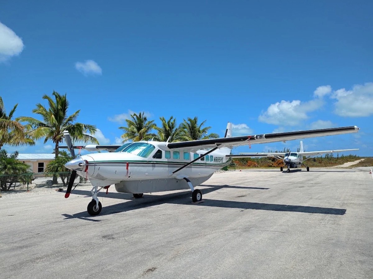 Two turboprop aircraft parked on the Chub Cay airstrip among palm trees